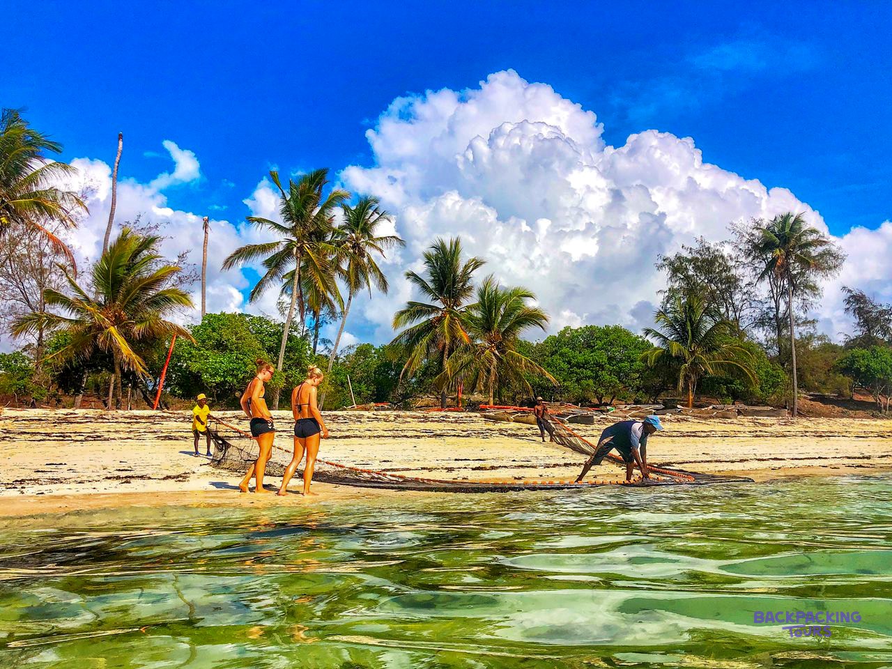 Two volunteers walk a palm fringed beach while a fisherman works at the water's edge.