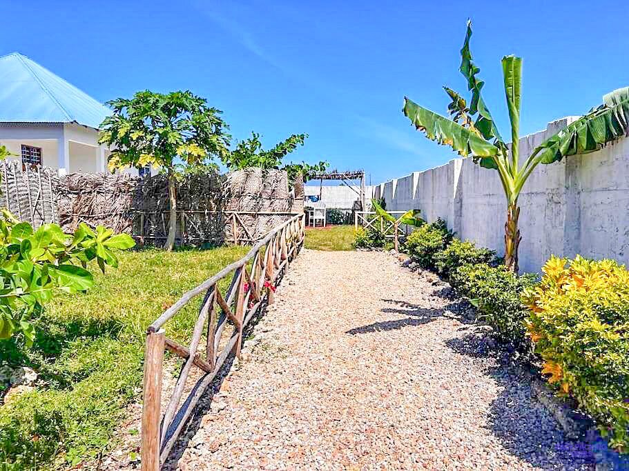 A gravel path edged with rustic railings runs between banana plants and the house.
