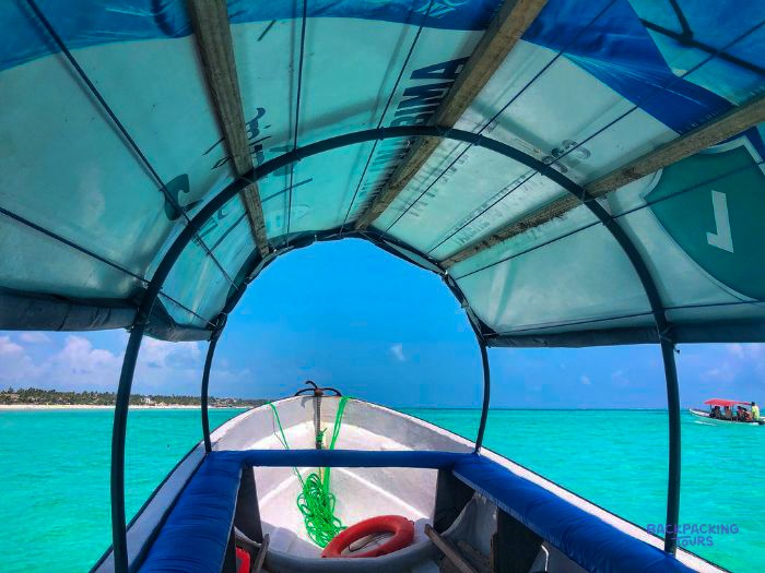 The blue canopy of a small boat frames bright turquoise water and the low green shore.