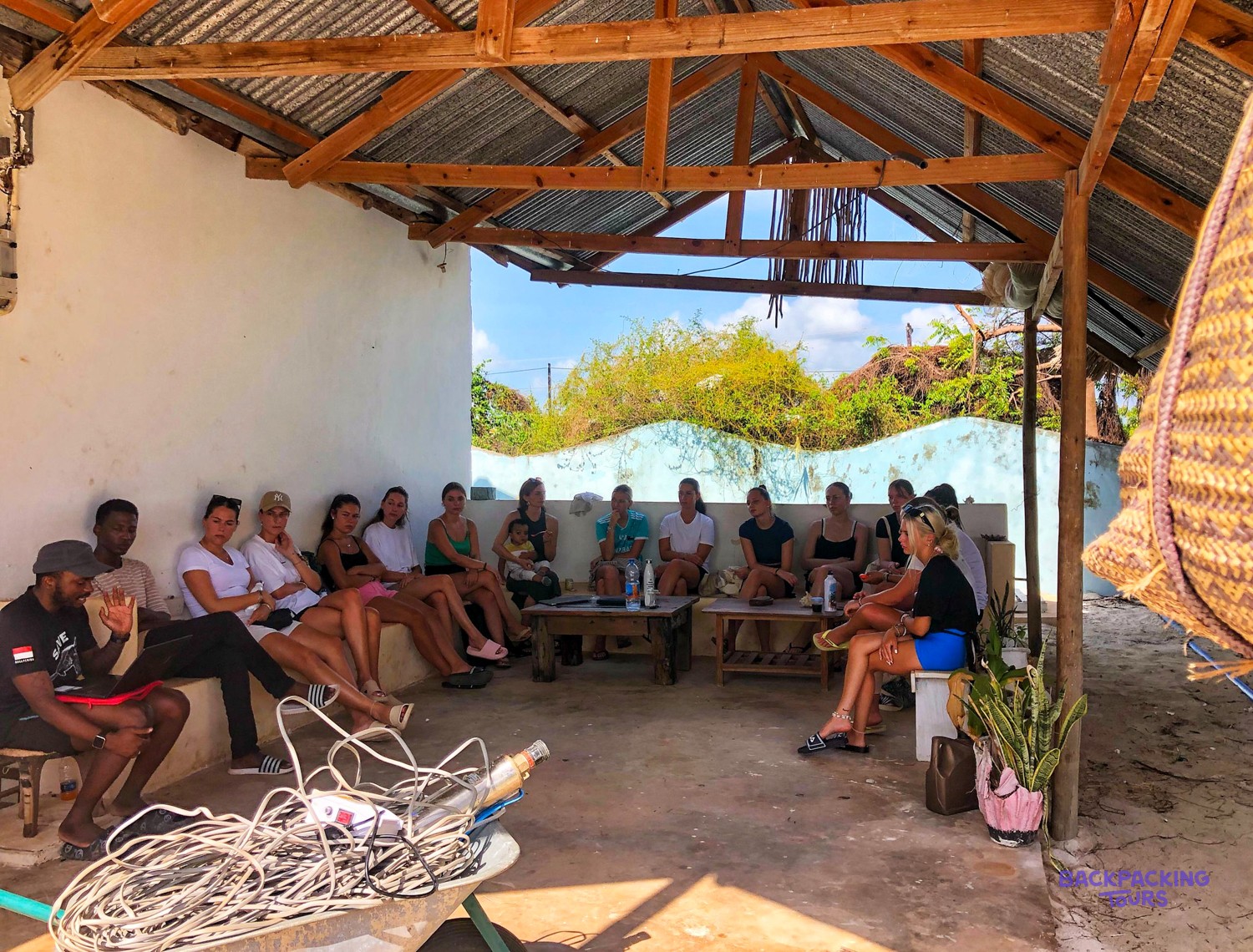 Volunteers and local staff sit together under a shelter for a briefing.