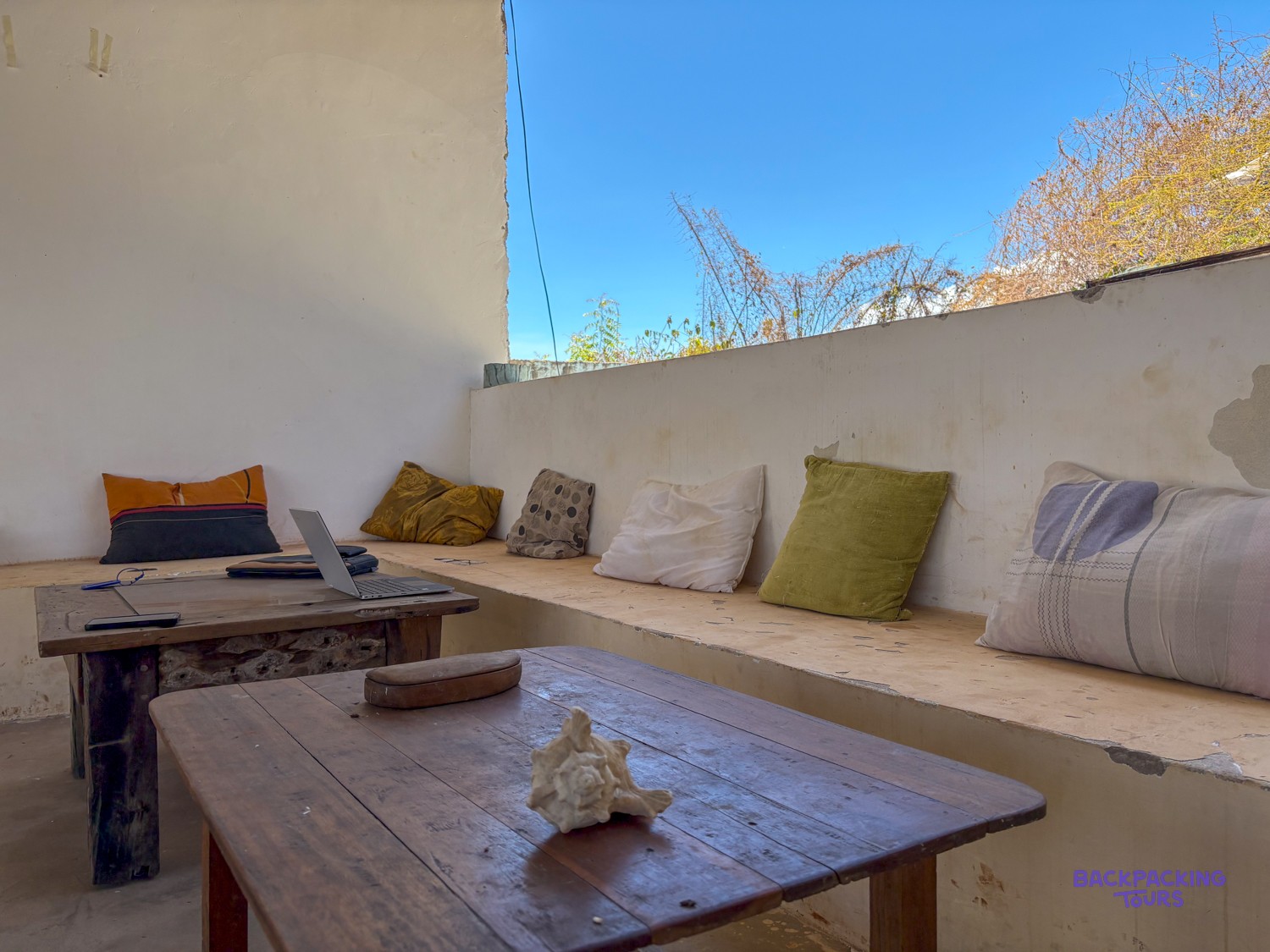 Cushioned benches and low wooden tables in the shaded lounge of the volunteer house.