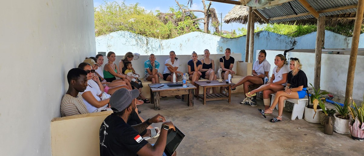 The group sits around the shaded courtyard of the volunteer house for a briefing.