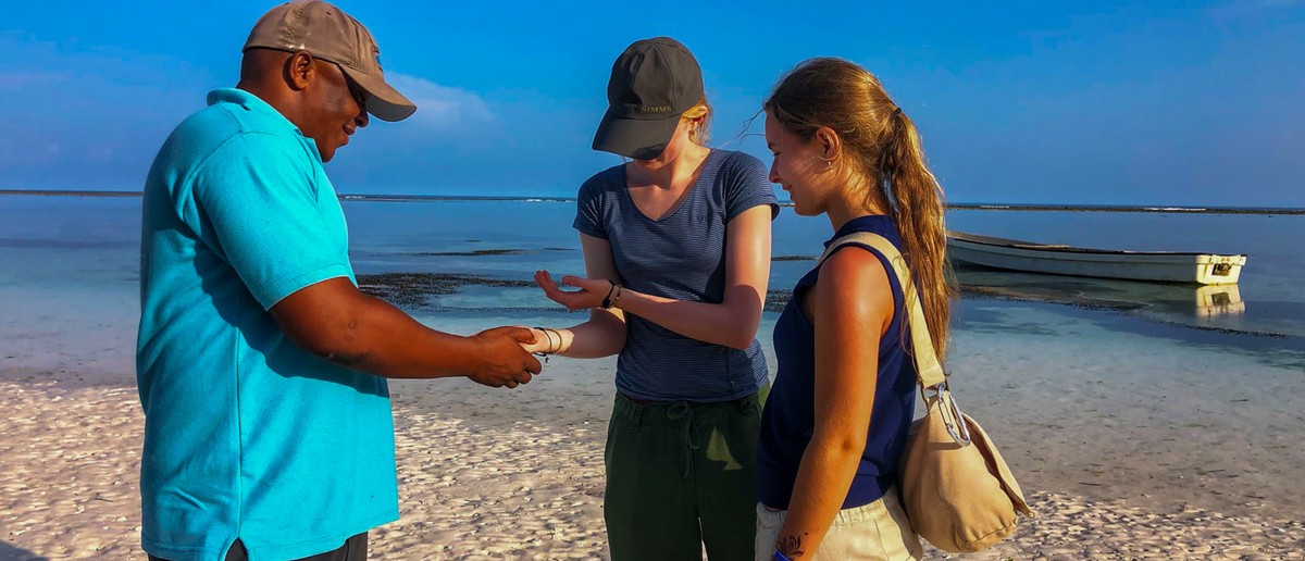 A local guide shows two volunteers something he has picked up from the shore.