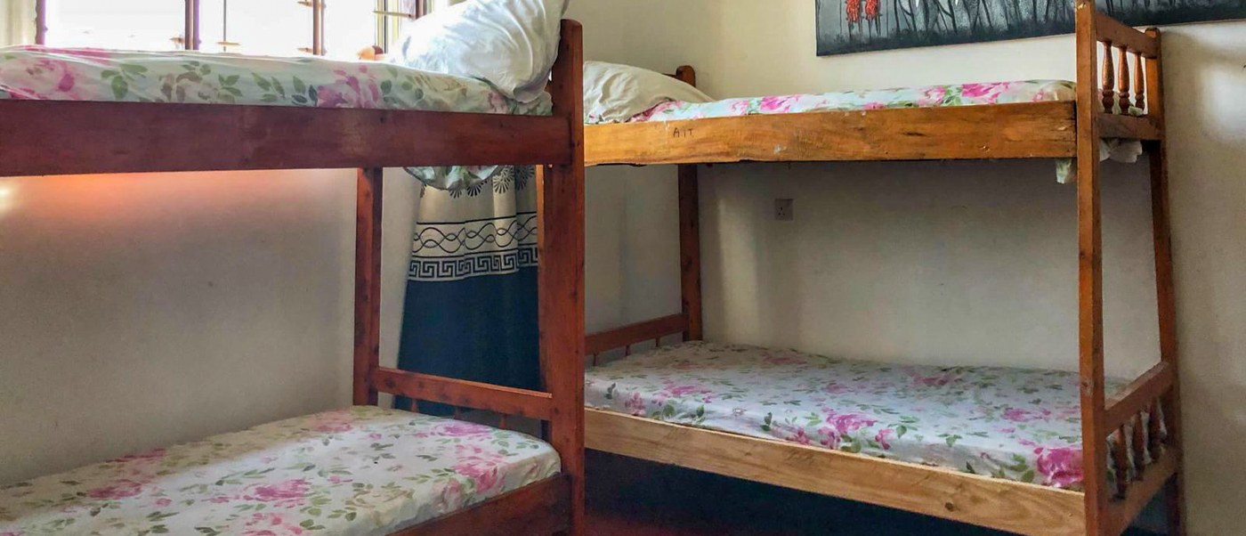 Two wooden bunk beds made up with floral bedding stand beside a bright barred window.