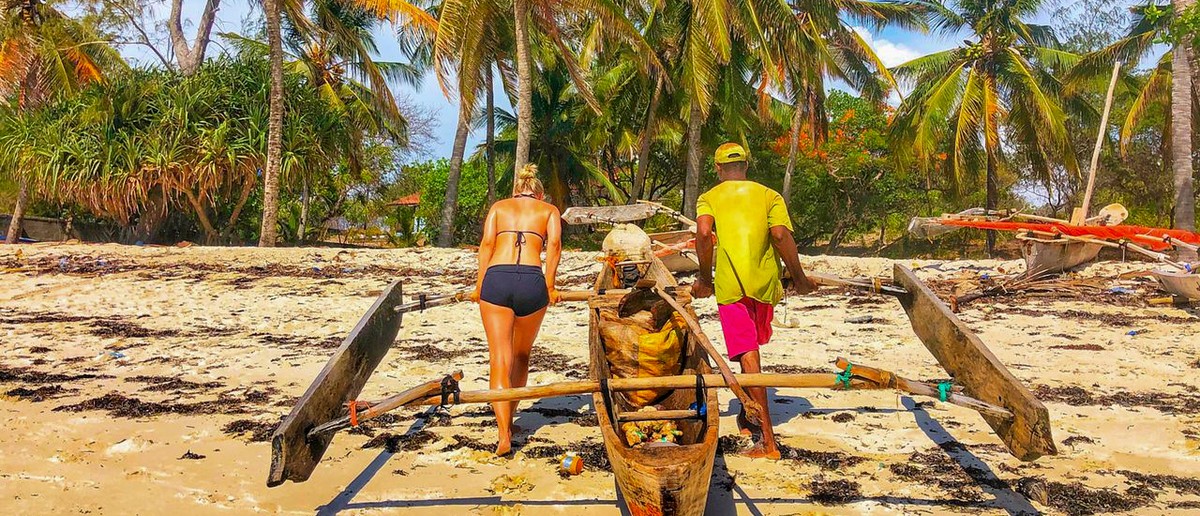 A fisherman and a volunteer move a loaded outrigger canoe down the sand towards the sea.