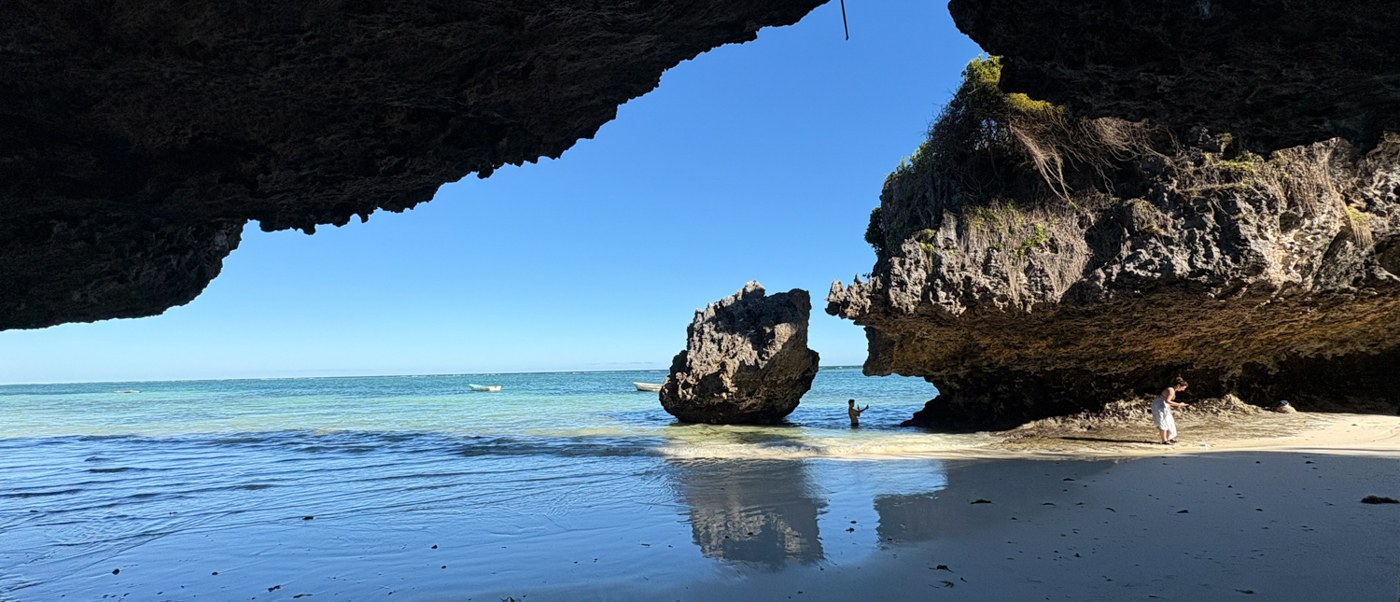 A swimmer wades past a sea stack in a cove framed by an undercut coral cliff.