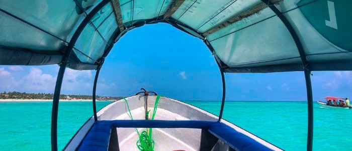 The blue canopy of a small boat frames bright turquoise water and the low green shore.
