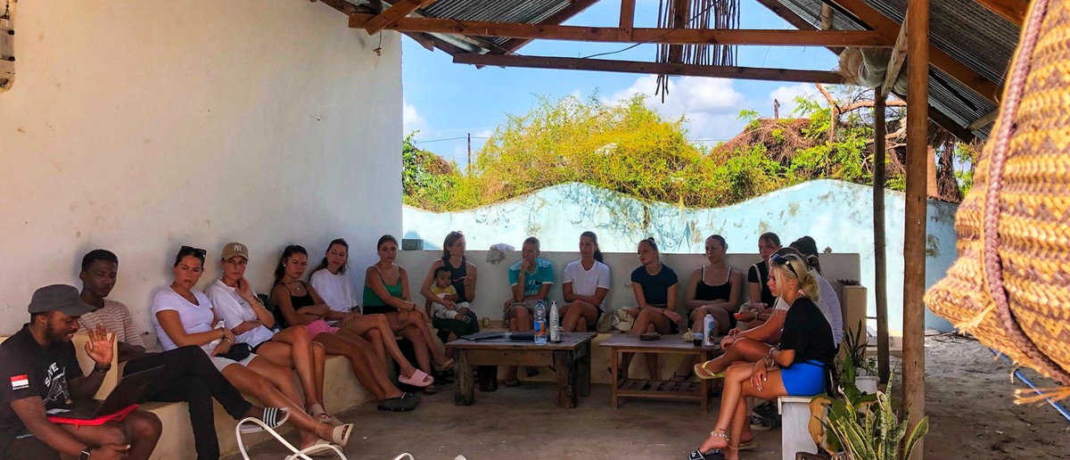 Volunteers and local staff sit together under a shelter for a briefing.
