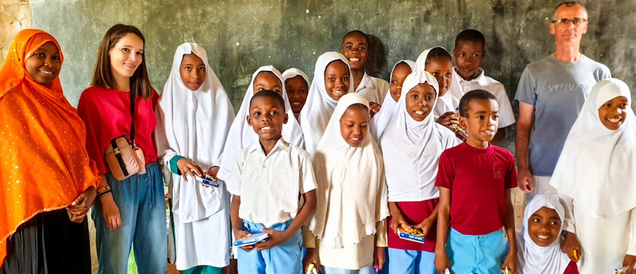 Smiling children and adult volunteers pose together in a classroom in Zanzibar.
