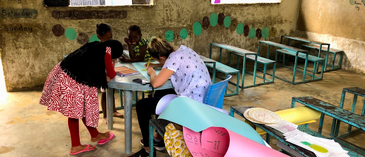 A volunteer teacher helps three young students with an art activity in a classroom in Zanzibar.