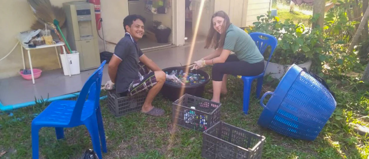 Two smiling volunteers sorting plastic bottles for environmental conservation in Pranburi, Thailand.