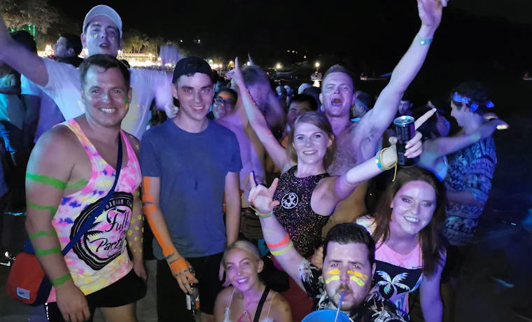 Backpackers with neon paint and glow sticks enjoying the energetic Full Moon Party on Koh Phangan.