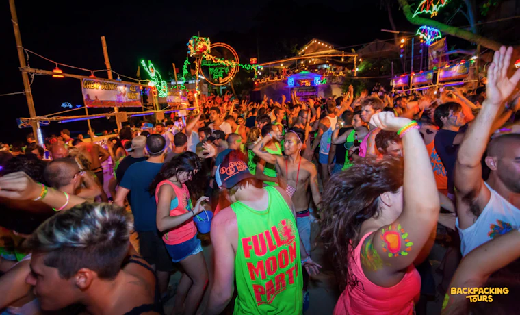 Energetic partygoers dance under vibrant neon lights at the famous Full Moon Party on Koh Phangan.