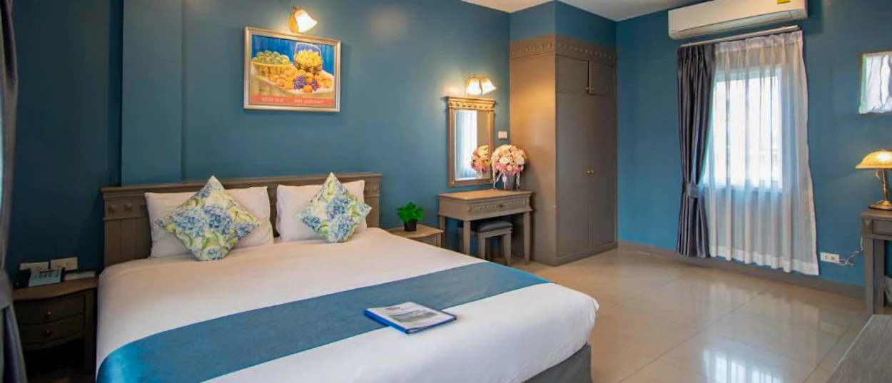 A comfortable hotel room in Chiang Mai featuring a large bed, blue walls, and a window.