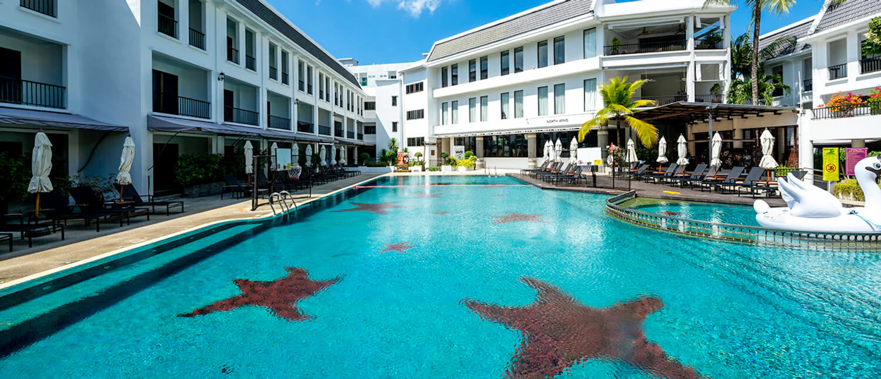 Bright blue resort swimming pool with starfish designs, surrounded by white buildings and palm trees in Phuket.
