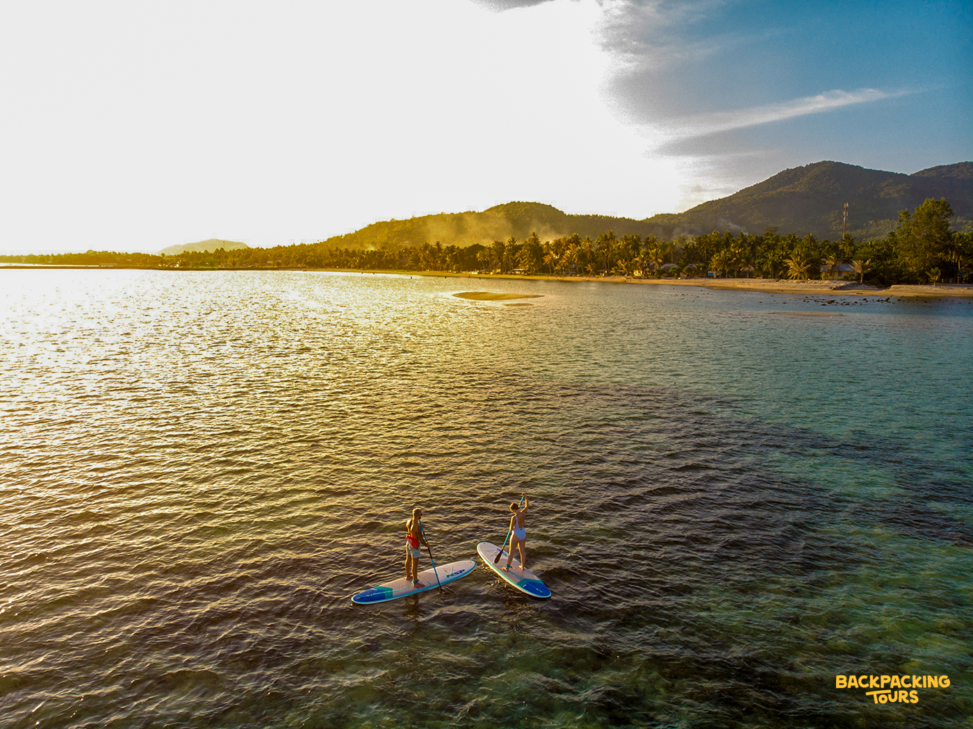 Paddleboarding on calm water at sPaddleboarding on calm water at sunset in Koh Phangan with mountains in the background during the beach day of the tourunset in Koh Phangan with mountains in the background during the beach day of the tour