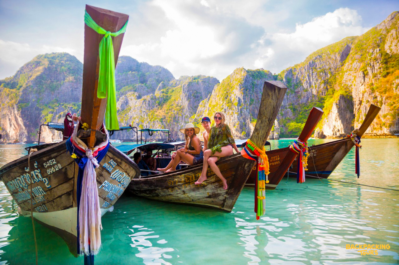 Traditional longtail boats anchored in Maya Bay with limestone cliffs in the background during the backpacking group's island tour