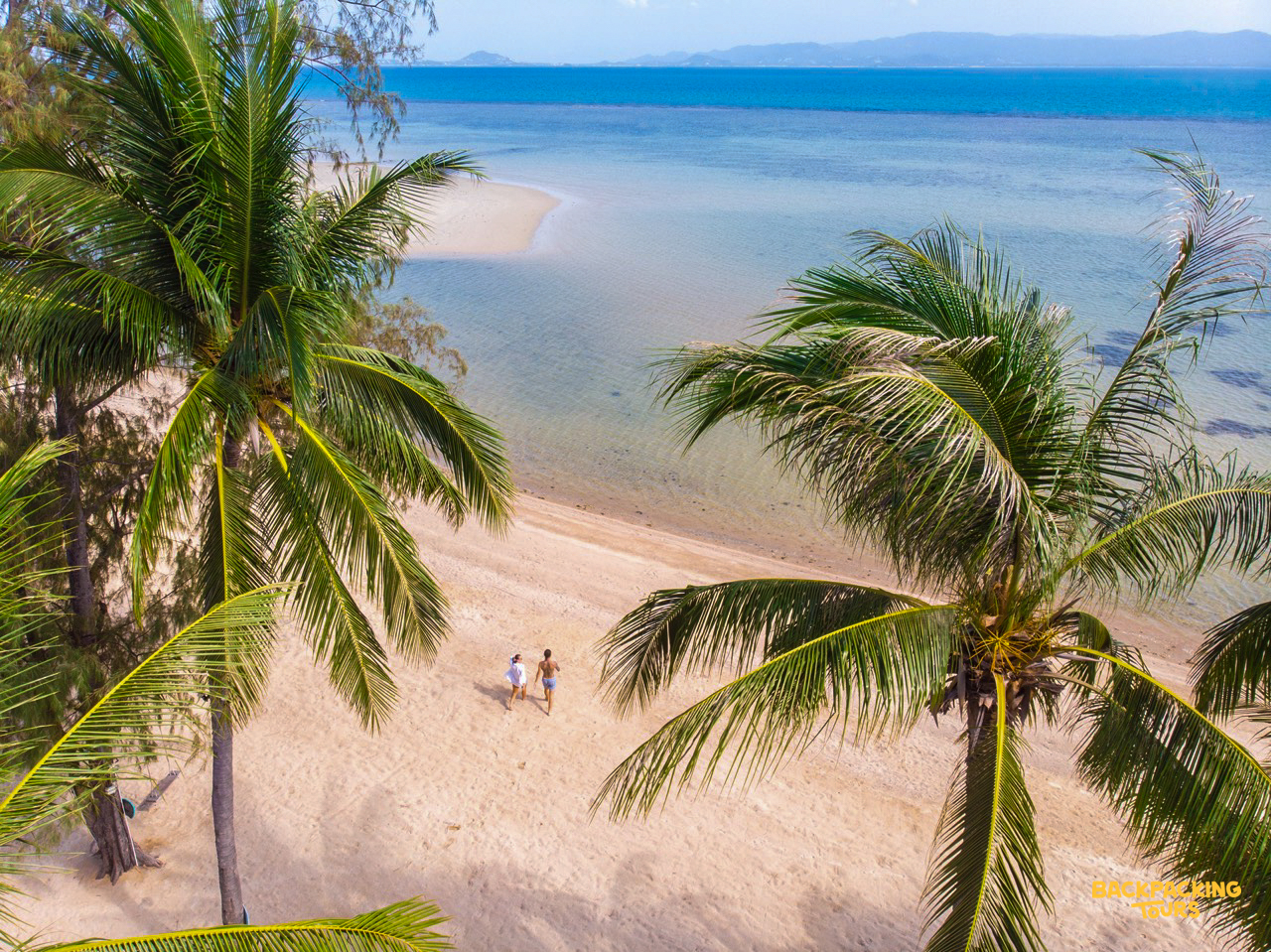 Drone view of coconut palms and sandy beach on Koh Phangan during a relaxing beach day on the backpacking tourPaddleboarding on calm water at sunset in Koh Phangan with mountains in the background during the beach day of the tour