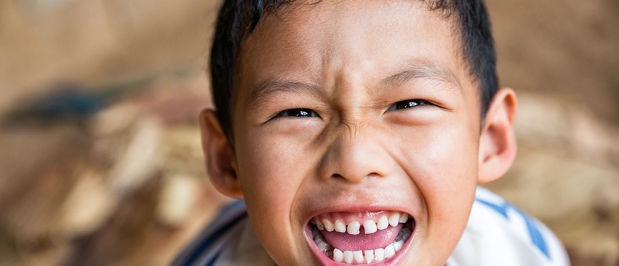 A young boy from a hill tribe community in Chiang Mai smiles joyfully at the camera.