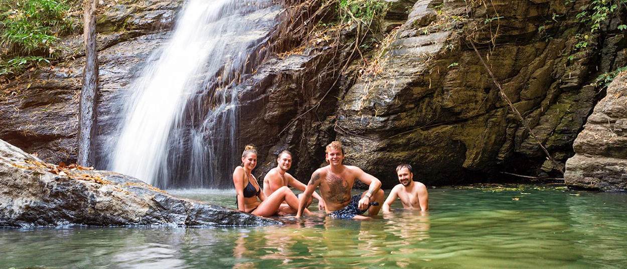 Smiling friends cool off in a natural pool beneath a waterfall in Chiang Mai.