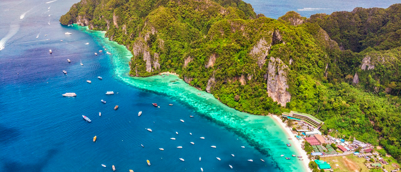 Drone view of boat touring Phi Phi Leh with turquoise water and lush cliffs