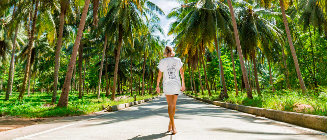 Backpacking tour participant walking along palm-lined road in Koh Phangan during yoga morning