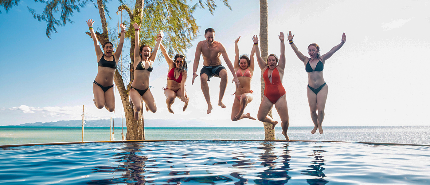 Backpacking tour friends jumping into pool at Koh Phangan beach resort during beach dayBackpacking tour friends playing beach volleyball at Koh Phangan during beach day