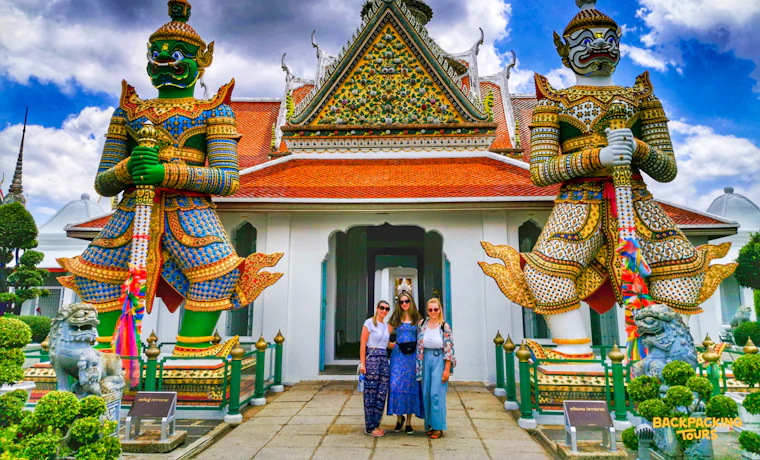 Three friends pose in front of a vibrant Thai temple with giant guardian statues in Bangkok.
