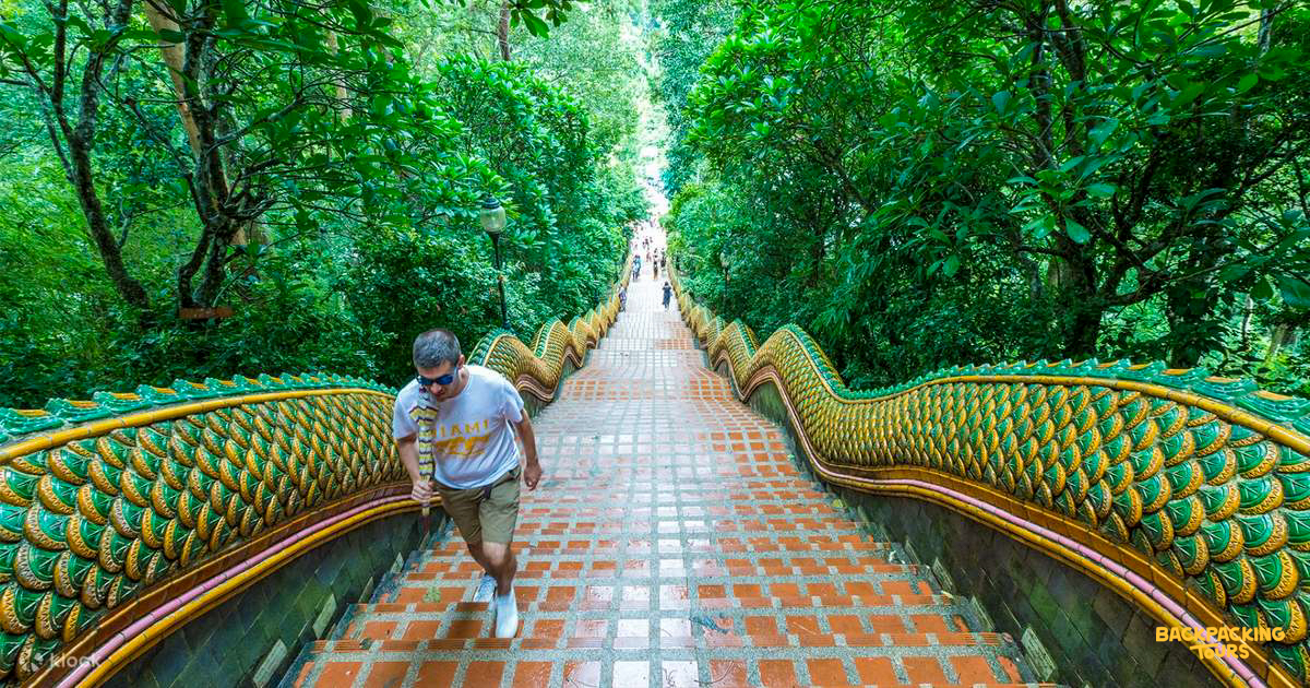 A man climbs the ornate Naga staircase at Doi Suthep temple, surrounded by lush greenery.