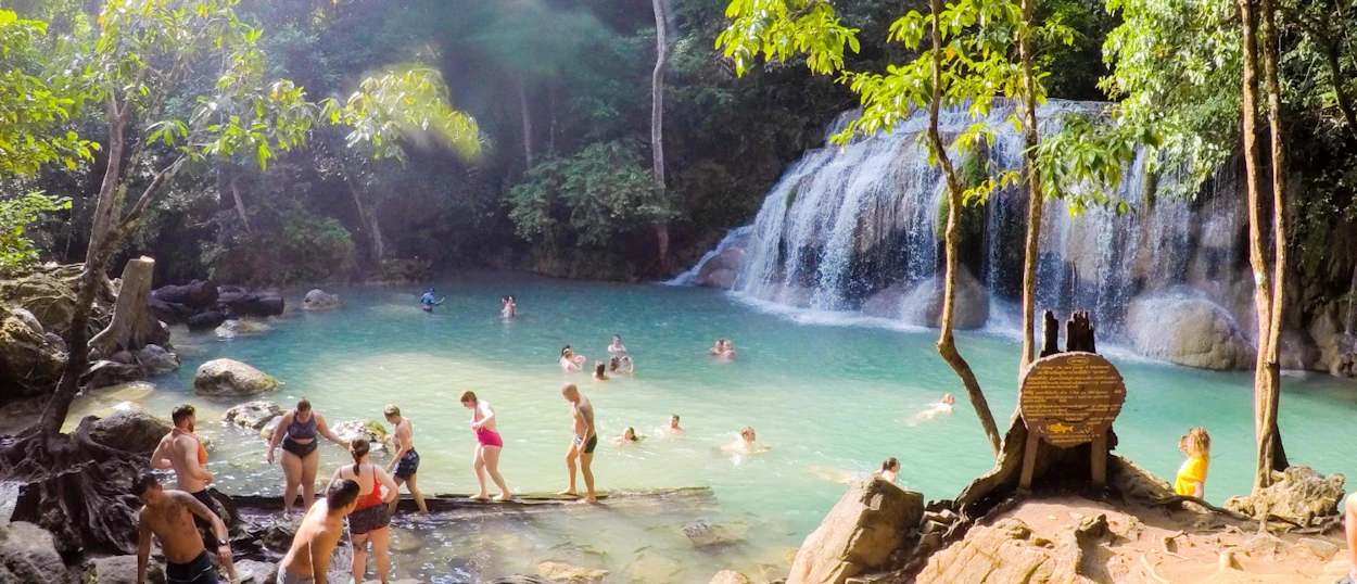 Visitors swim and relax in the refreshing emerald pools of Erawan Waterfalls, Thailand, amidst lush greenery.