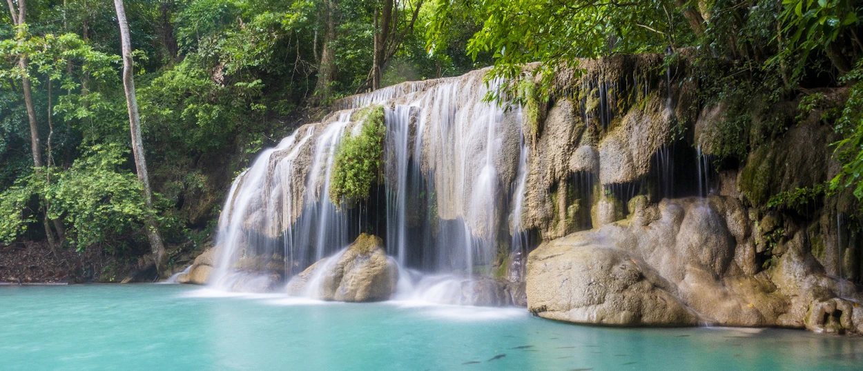 Beautiful Erawan Waterfall flowing into clear turquoise pools amidst dense green jungle in Thailand.