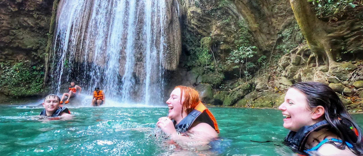 Happy travelers swim in the emerald pool at Erawan Waterfalls, surrounded by lush jungle.