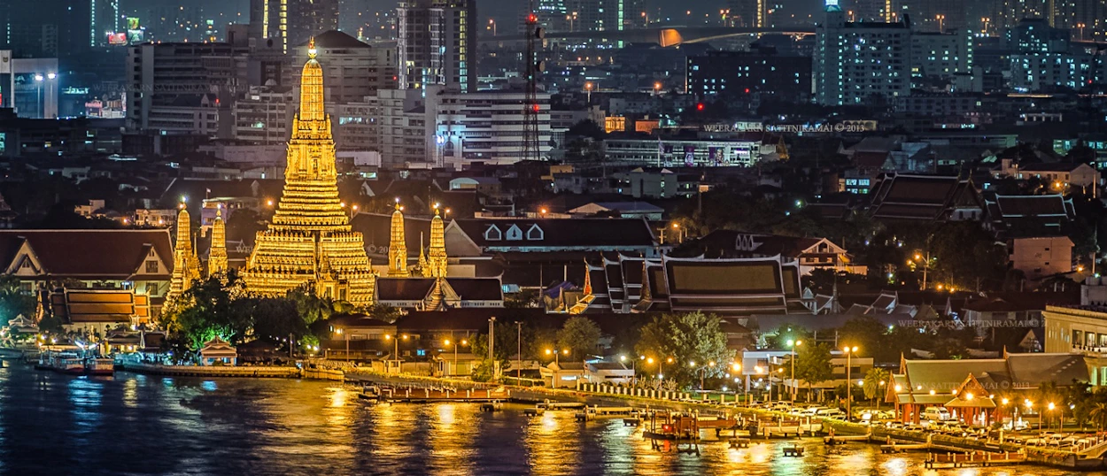 The illuminated Wat Arun temple stands majestically by the Chao Phraya River at night in Bangkok.