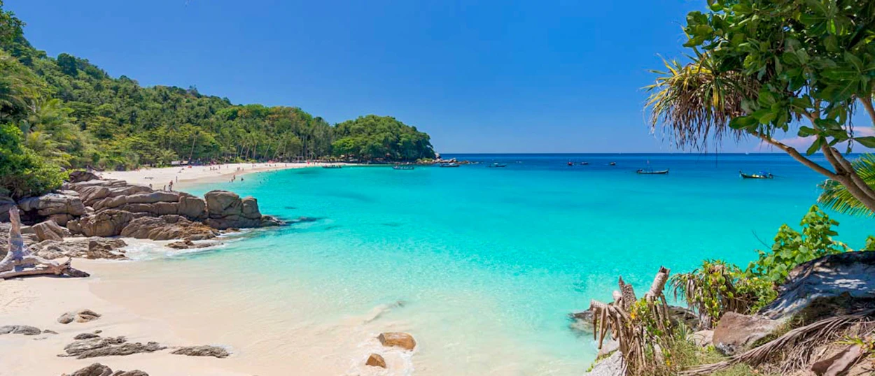 Idyllic Phuket beach with pristine white sand, clear turquoise sea, and verdant tropical foliage.