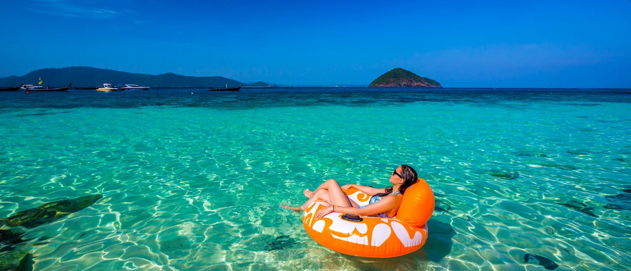 A woman floats on an orange tube in clear turquoise waters near a tropical island in Phuket.