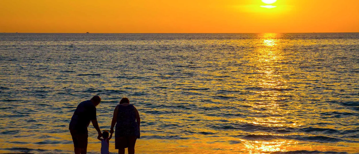 A family of three enjoys a serene golden sunset on a beautiful beach in Phuket.