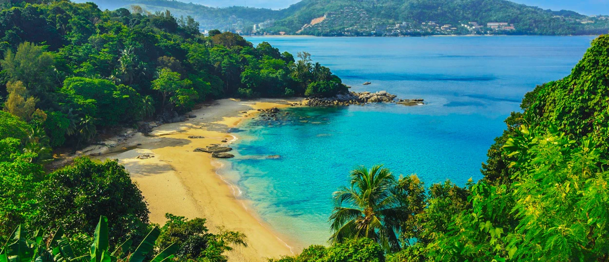 Beautiful Phuket beach from above, featuring clear turquoise water, golden sand, and dense green jungle.