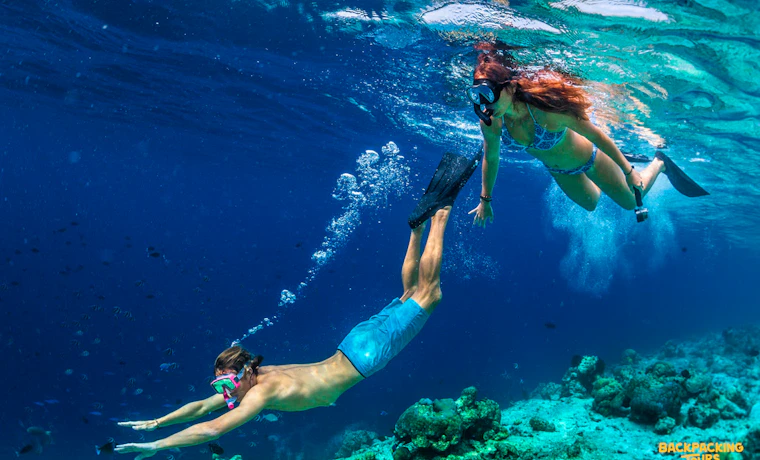 Two people snorkel and freedive in the clear blue waters of Koh Phangan.