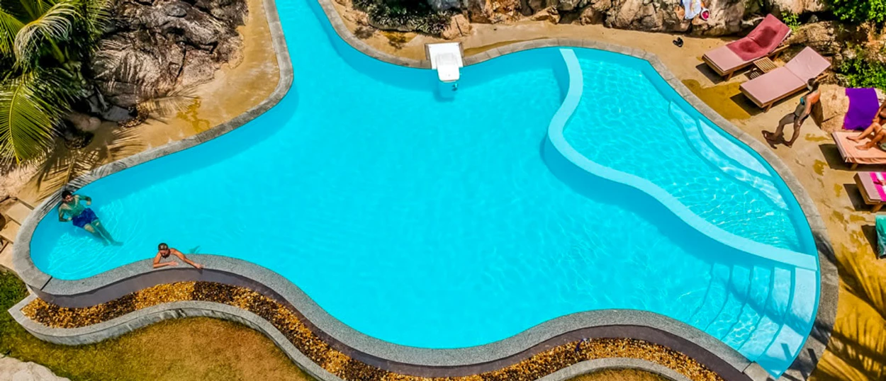 Aerial view of a bright blue resort swimming pool with two people relaxing in Koh Tao, Thailand.