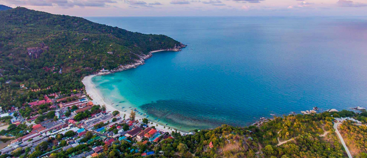 Vibrant turquoise waters meet a white sand beach, framed by lush green hills on Koh Phangan.