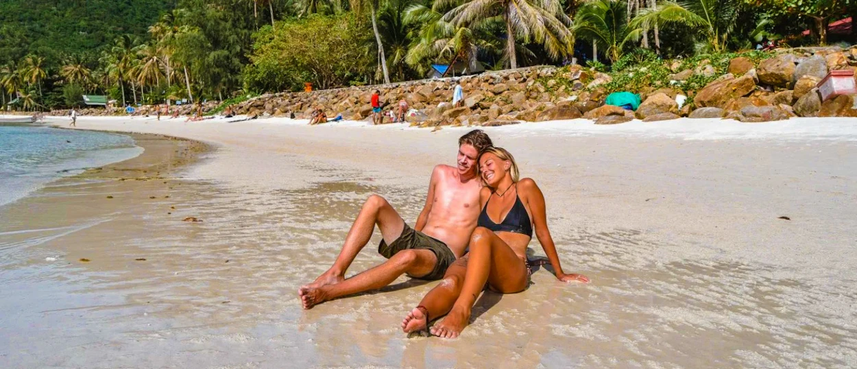 A happy couple relaxes on a beautiful sandy beach with palm trees in Koh Samui.