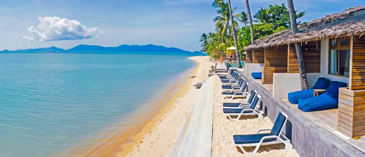 Relaxing tropical beach in Koh Samui with charming bungalows, lounge chairs, and clear turquoise water.