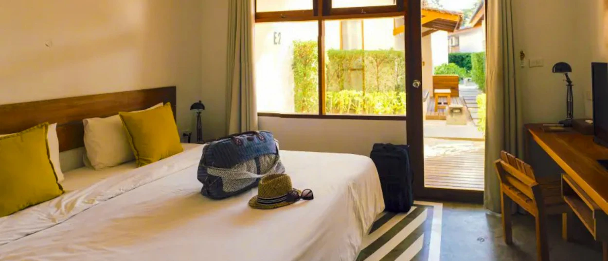 A bright resort room in Koh Samui with a large bed, luggage, and open patio door.