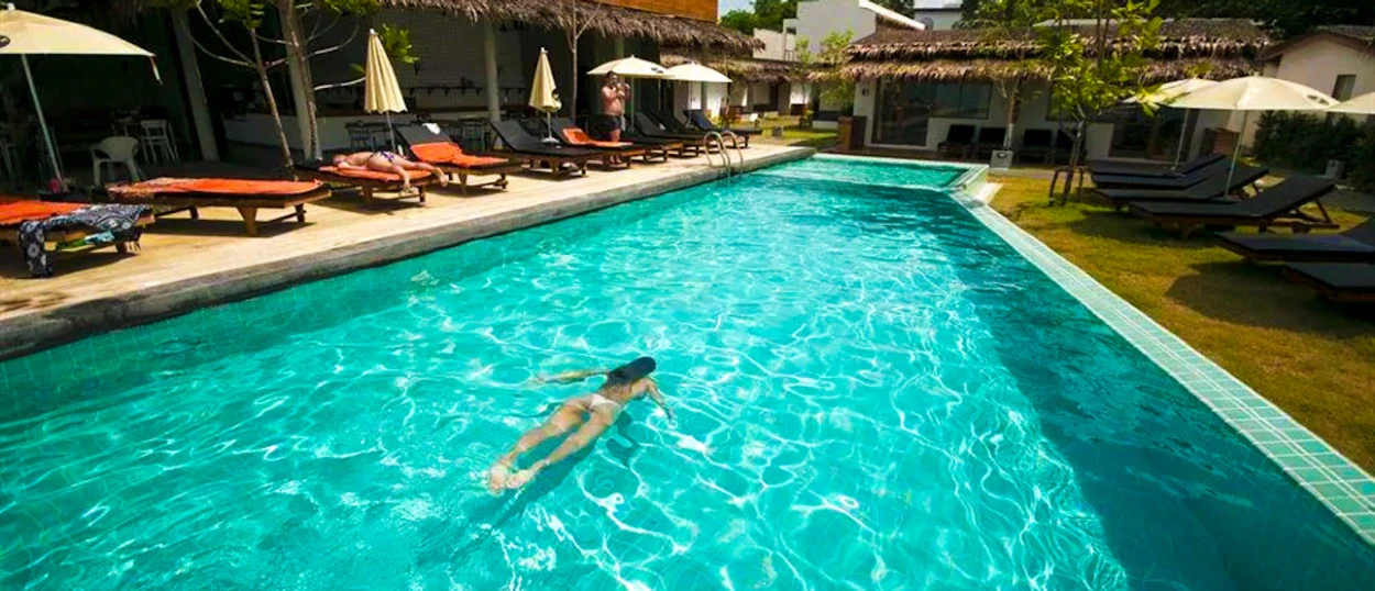 Relaxing at a resort pool in Koh Samui, a woman swims in the clear turquoise water.