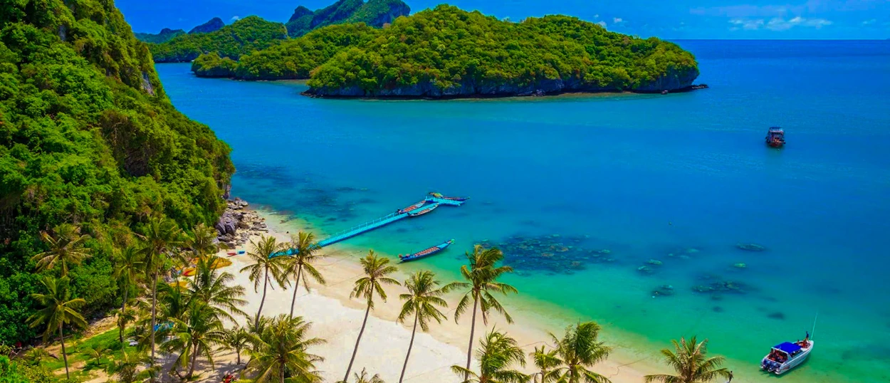 Stunning tropical beach with white sand, palm trees, clear water, and green islands in Koh Samui.