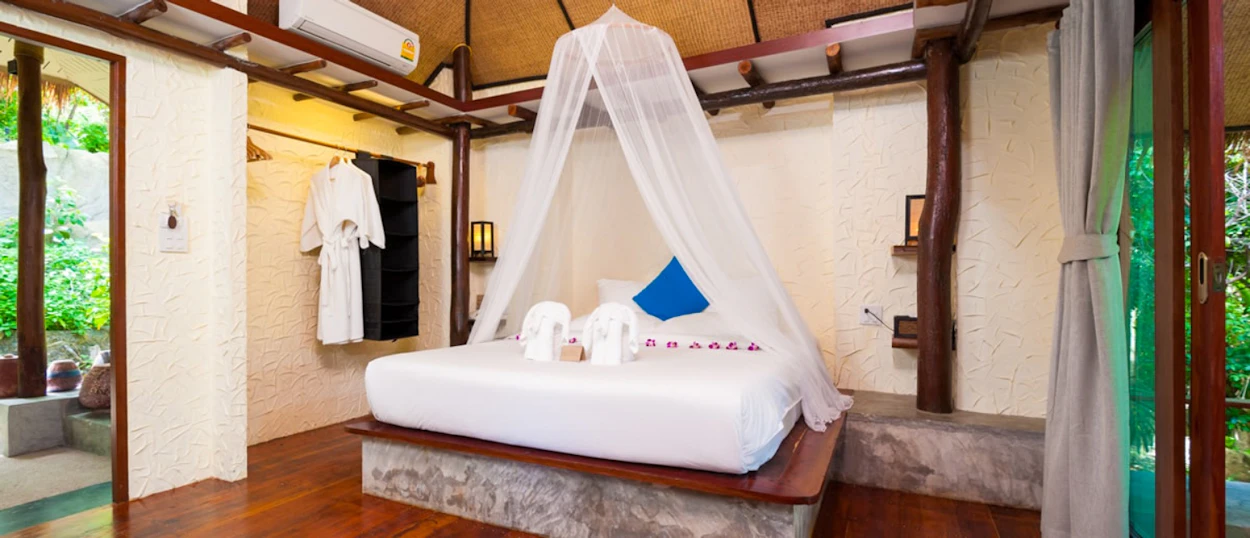 Relaxing resort bedroom on Koh Tao with a canopy bed, bathrobes, and tropical garden access.