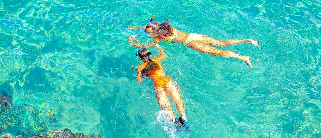 Two women snorkel in the crystal clear turquoise waters of Koh Tao, Thailand.