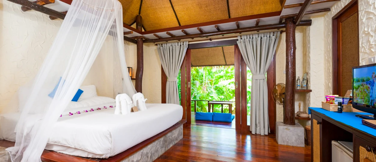 Comfortable resort room in Koh Tao with a canopy bed and open doors to lush tropical greenery.