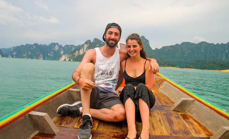 Two smiling travelers on a longtail boat, exploring the stunning Khao Sok National Park.