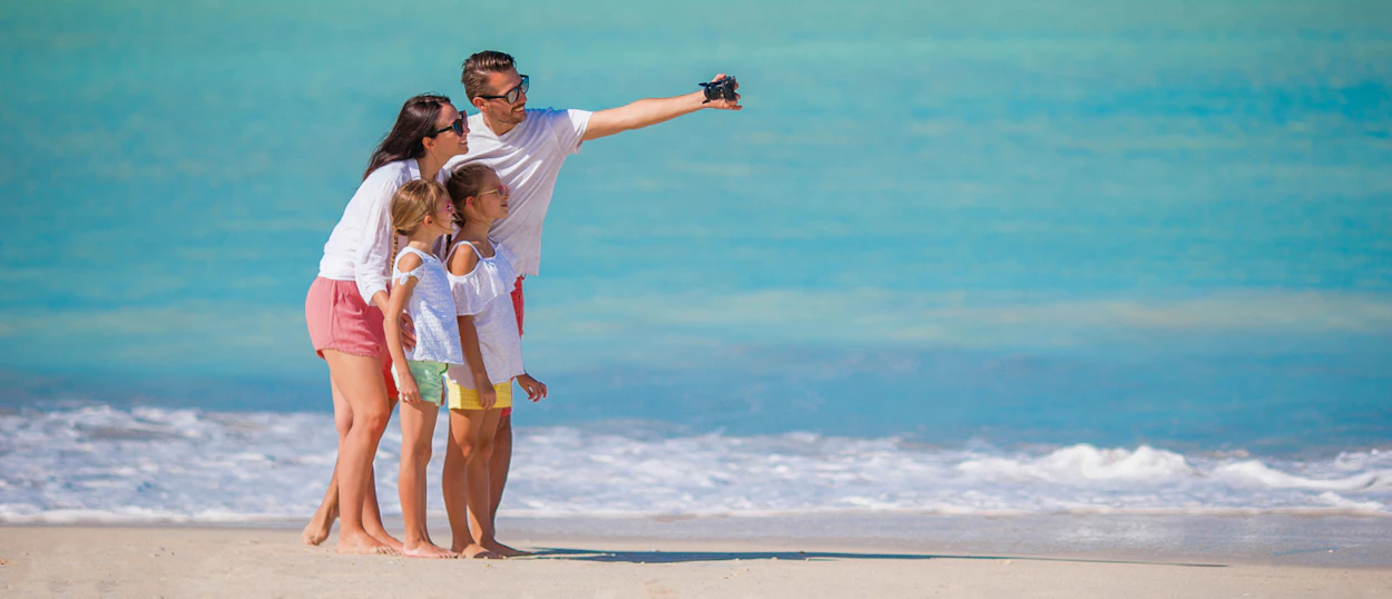 A happy family takes a selfie on a beautiful sandy beach with turquoise water in Phuket.